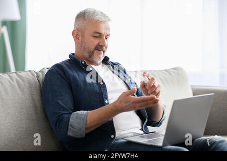 Mature man using disinfectant spray for cleaning hands, using laptop Stock Photo