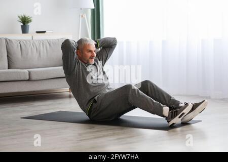 Athletic bearded senior man doing exercises for abs at home Stock Photo