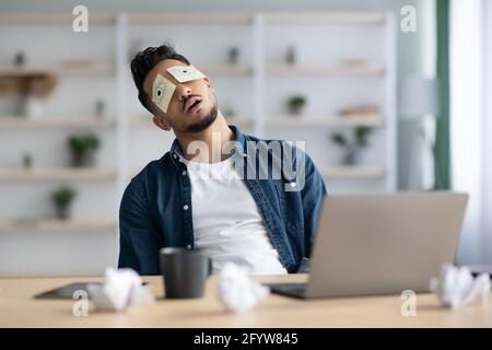 Tired arab guy with eyes drawing sleeping at workdesk Stock Photo