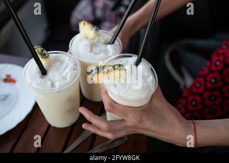 Woman's hands holding three cocktails in plastic glasses with black straws Stock Photo