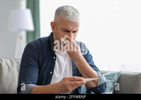 Sick elderly man sneezing and checking body temperature Stock Photo
