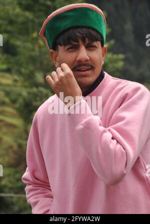 Selective focus of a good looking young guy touching his mustache and standing outdoor with looking at camera, Portrait shot of a young men with wearing himachali topi (Himachali traditional cap) Stock Photo