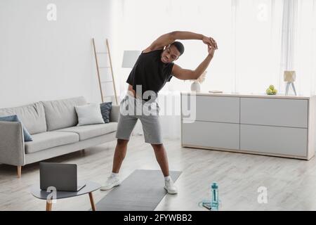 Black Guy Exercising Near Laptop Doing Side Bend Stretching Indoor Stock Photo