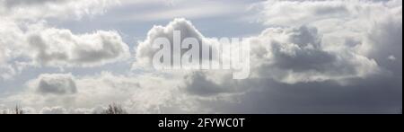 Panorama with well defined cumulus cloud chased by dramatic dark rain filled front in dramatic sky scenery landscape. Stock Photo
