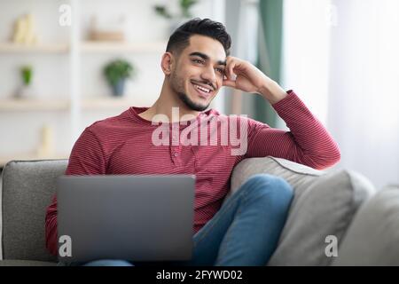 Dreamy arab guy sitting on sofa with laptop Stock Photo