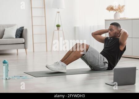 Side-View Of African American Guy Doing Sit-Ups At Laptop Indoor Stock Photo