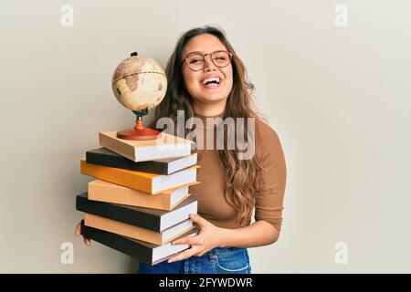 Young hispanic girl studying geography smiling and laughing hard out loud because funny crazy joke. Stock Photo