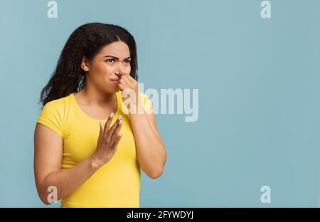 African american woman plugging her nose, smelling something stinky and unpleasant on blue background, copy space Stock Photo