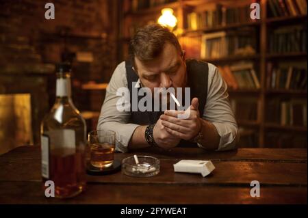 Man smokes cigarette and drinks alcohol beverage Stock Photo
