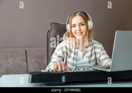 Woman in headphones learn to play piano online using laptop at home interior. Woman play synthesizer piano during online lesson with teacher.Teenager Stock Photo