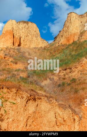 Landscape view clay cape cliffs. Green grass, lawns grown on slopes of clay mountains against blue sky. Hills of mountain and slopes of cape are Stock Photo