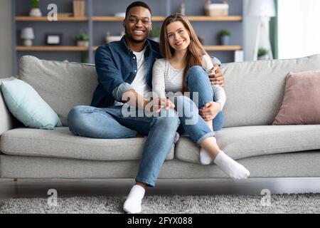 Portrait Of Happy Young Interracial Spouses Posing On Couch At Home Stock Photo