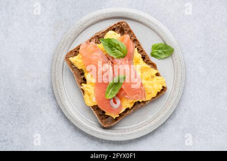 Breakfast toast with scrambled eggs and smoked salmon Lox on grey plate, top view. Isolated on grey concrete background. Tasty healthy sandwich with e Stock Photo