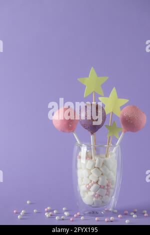 colorful cake pops in a glass with marshmallows on a purple background with sprinkles. festive, birthday background. vertical image. copy space. Stock Photo