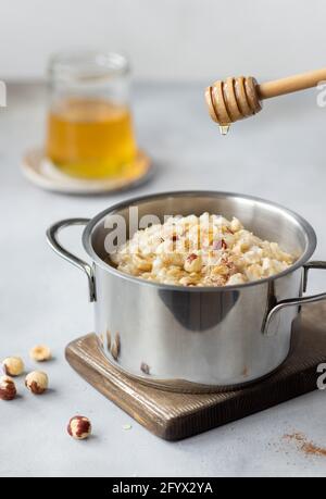 honey dripping from wooden honey dipper into pan with oatmeal porridge, topped with hazelnuts and cinnamon. clean eating concept. vertical image. Gray Stock Photo