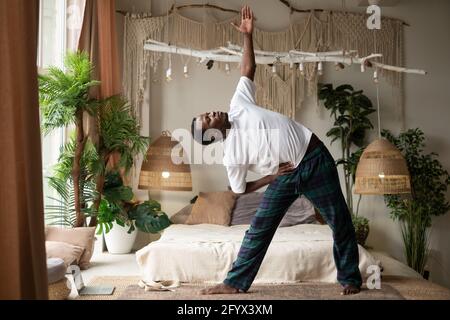 African man practicing yoga doing trikonasana or triangle pose at home Stock Photo