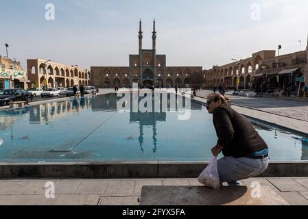 Male person sits down on a bench with view on the big pool and mosque on Amir Chakhmaq Square. Yazd, Yazd Province, Iran. Stock Photo