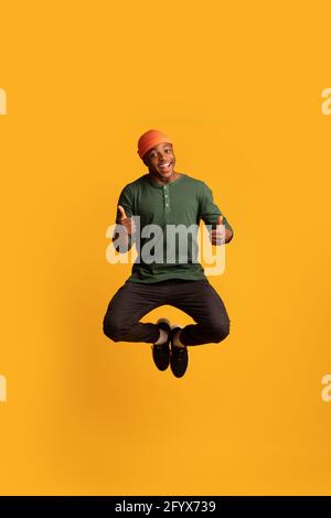 Joyful Black Hipster Guy Jumping In Air And Showing Thumbs Up Stock Photo