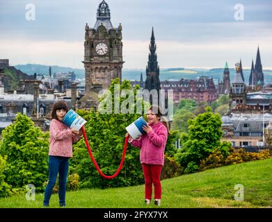 Two young girls pretend to communicate with giant connected tin cans launching Edinburgh Science Festival, Calton Hill with city skyline, Scotland, UK Stock Photo