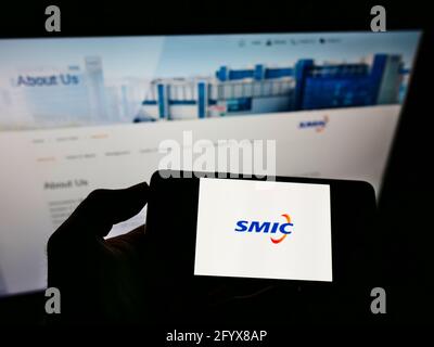 Person holding smartphone with logo of Semiconductor Manufacturing International Corporation on screen in front of website. Focus on phone display. Stock Photo
