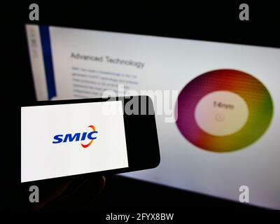 Person holding cellphone with logo of Semiconductor Manufacturing International Corporation on screen in front of web page. Focus on phone display. Stock Photo