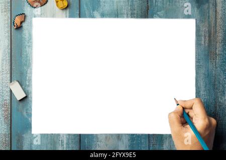 Top view of blank white paper page on blue wooden background with human hand holding pencil Stock Photo