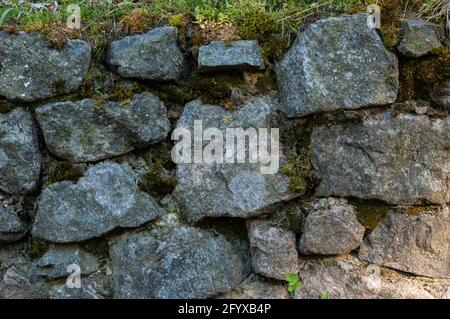 a wall of rough granite stones, with moss in the cracks Stock Photo