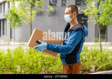 Postal delivery courier man wearing protective face mask in front of cargo van delivering package holding box due to Coronavirus disease or COVID-19 Stock Photo