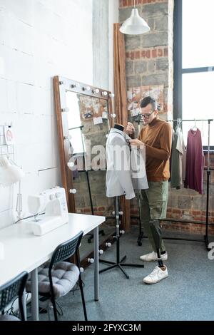 Disable man with leg prosthesis working over new jacket while standing by dummy Stock Photo