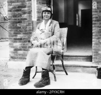 Portrait of Margaret Holmes (née Margaret Elisa Oliver, 1879-1968), wife of traveler, photographer and filmmaker Elias Burton Holmes wears an aviator hat and goggles and holds a bag in her lap as she sits waiting for a flight from France to Morocco, 1923. (Photo by Burton Holmes) Stock Photo