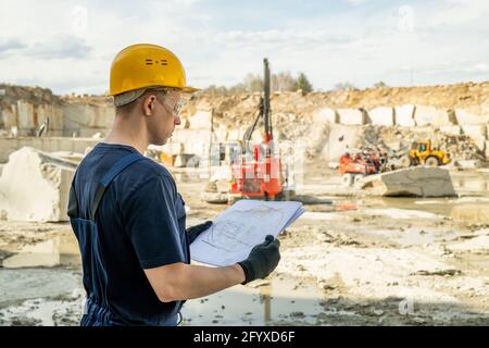 Young builder in workwear holding sketch of construction Stock Photo
