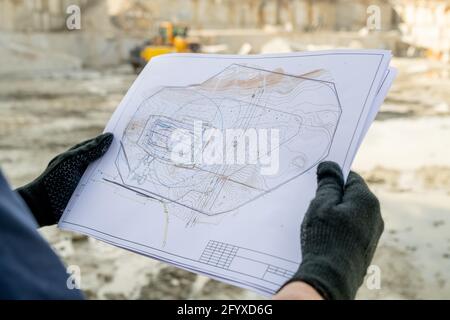 Gloved hands of builder holding paper with sketch of construction Stock Photo