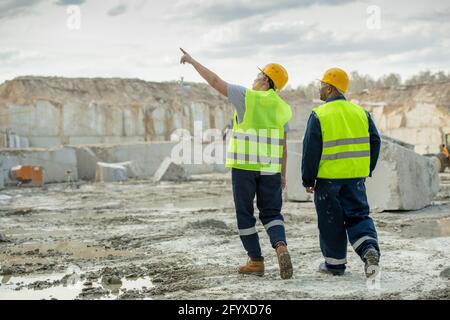 Two male workers in uniform discussing features of construction site Stock Photo