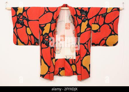 Women's Haori with abstract pattern. Haori for a woman with an ornament over the entire plane of irregular orange and yellow surfaces with round shapes, surrounded by black lines and scattered white motifs. Fine crepe silk (Kinsha) with a damask woven motif (Rinzu) of Kris-Kras lines and tie-dye decoration (Shibori). Fenciled silk lining. Stock Photo