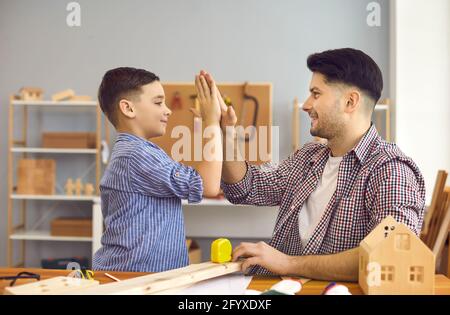 Happy smiling father giving high five and support to son at home workshop Stock Photo