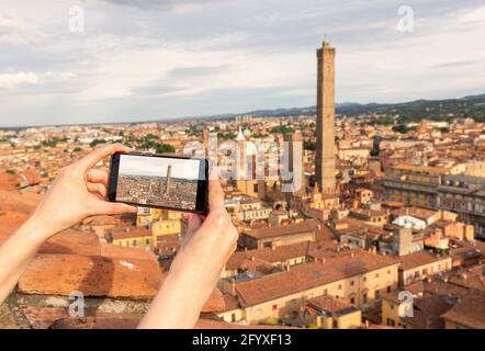 travel concept - tourist takes picture of Due Torri -two tower - symbol of city in Bologna, Italy on smartphone