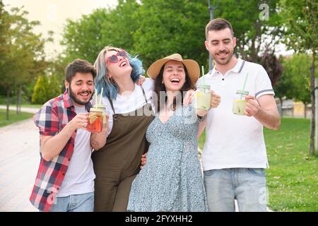 Group of happy friends drinking refreshing drinks and having fun in a park on a sunny summer day. Stock Photo