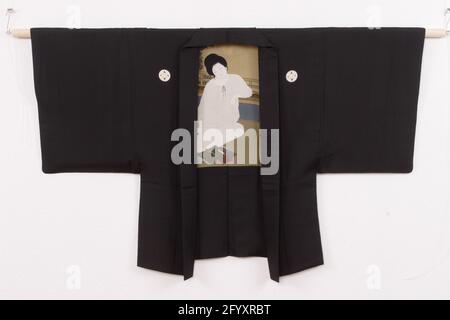 Men's Haori with a 'study of elegance'. Haori for a man with an adornment at the lining of a sunken sitting in mind on a window overlooking a veranda, tree and moon, with books, paper and an easel around her. One of the books bears the title 'Furyu Kenkyu' ('study of elegance'). At the bottom right in red the seal shoha. Black glossy silk (habutae) with hand-painted and stenciled yuzen decoration. Five family weapons (mon) of Shippo and Hanabishi motifs. Stock Photo