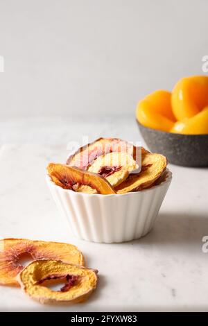 Peach chips in white bowl on light background, home drying. Snack vegan and children sugar free dessert. Vertical orientation. Close up. Stock Photo