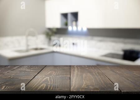 Empty wooden tabletop and defocused modern kitchen for design and display your products. Blured abstract kitchen background. Stock Photo