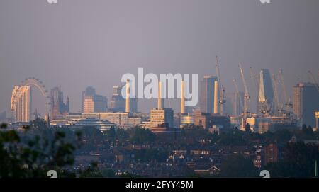 London, UK. 30 May 2021. Hazy evening sun strikes skyscrapers in central London as a mini-heatwave begins in the capital. The London Eye, Houses of Parliament and four chimneys at the former Battersea Power Station shimmer in evening heat in a long shot from 8 miles distance with the leafy suburbs of Wimbledon in the foreground. Credit: Malcolm Park/Alamy Live News. Stock Photo
