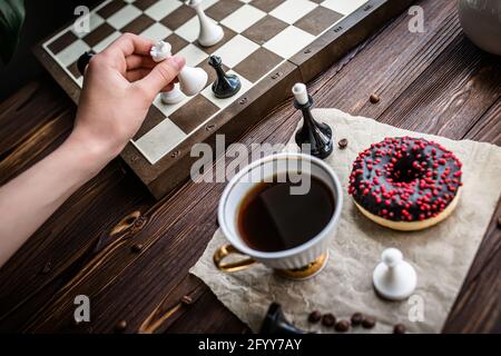 hand holds a white vintage cup of coffee. Chess board and scattered chess  on wooden table. Chocolate doughnut for morning breakfast. board game  Concep Stock Photo - Alamy
