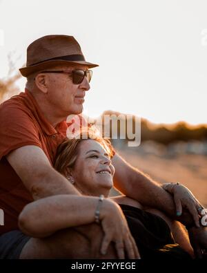 Content adult couple in summer wear embracing and resting on sandy seacoast during scenic sunset Stock Photo