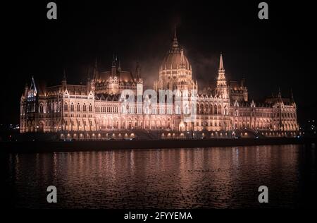 Exterior of grand Hungarian Parliament Building in Gothic and Renaissance styles illuminated by bright lights at night and located on Danube river sho Stock Photo