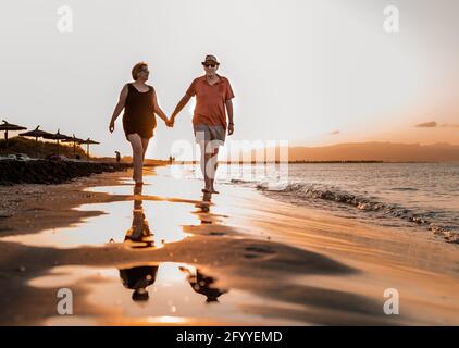 Couple in summer clothes holding hands and walking on sandy seacoast at sunset Stock Photo