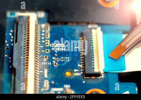 Connecting a flex cable to the laptop motherboard with tweezers, laptop repair in a service center Stock Photo