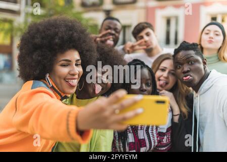 Content diverse partners with tongues out taking self portrait on cellphone on city street in daylight Stock Photo