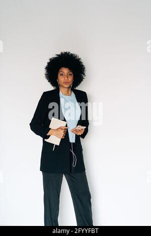 Elegant African American female with mobile phone and earphones looking at camera on white background Stock Photo
