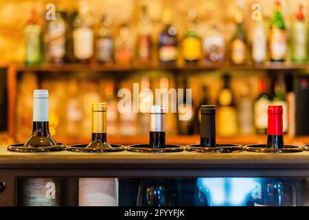 Glass bottles of red wine placed on bar counter in restaurant against blurred shelves with bottles of alcohol beverages Stock Photo