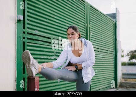Flexible young ethnic sportsWoman in activewear stretching legs after jogging on city street Stock Photo